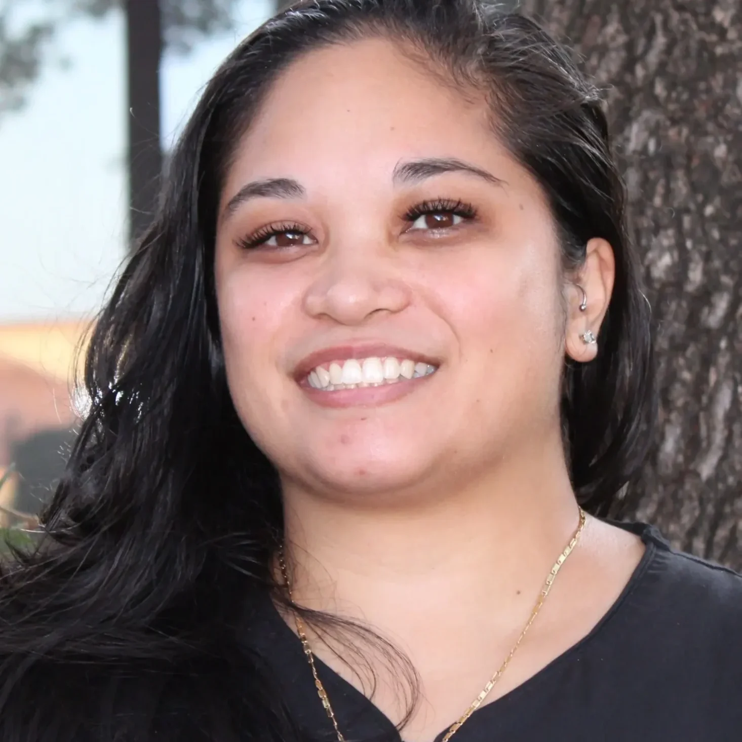 A woman smiling for the camera in front of a tree.