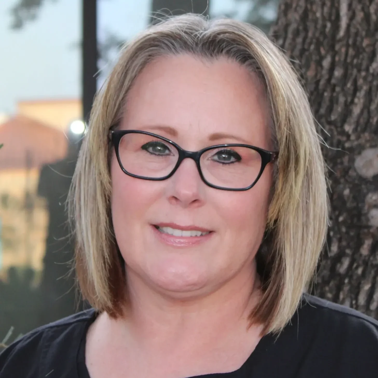 A woman with glasses standing in front of a tree.